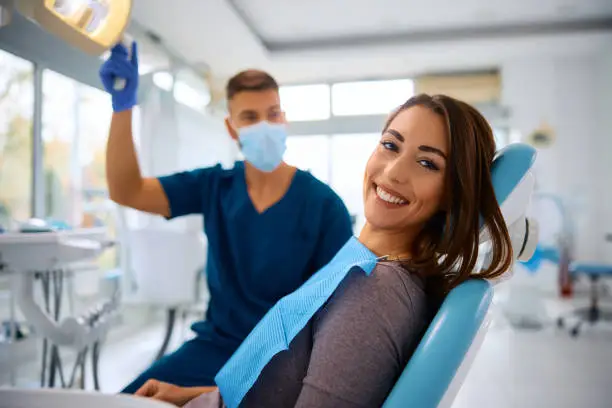 happy woman having dental treatment at dentists office and looking at camera